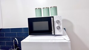 A microwave with a digital display and a control panel, placed on a white appliance with a blue tiled backsplash. - Comfy Studio 30min to Central London (Wembley)