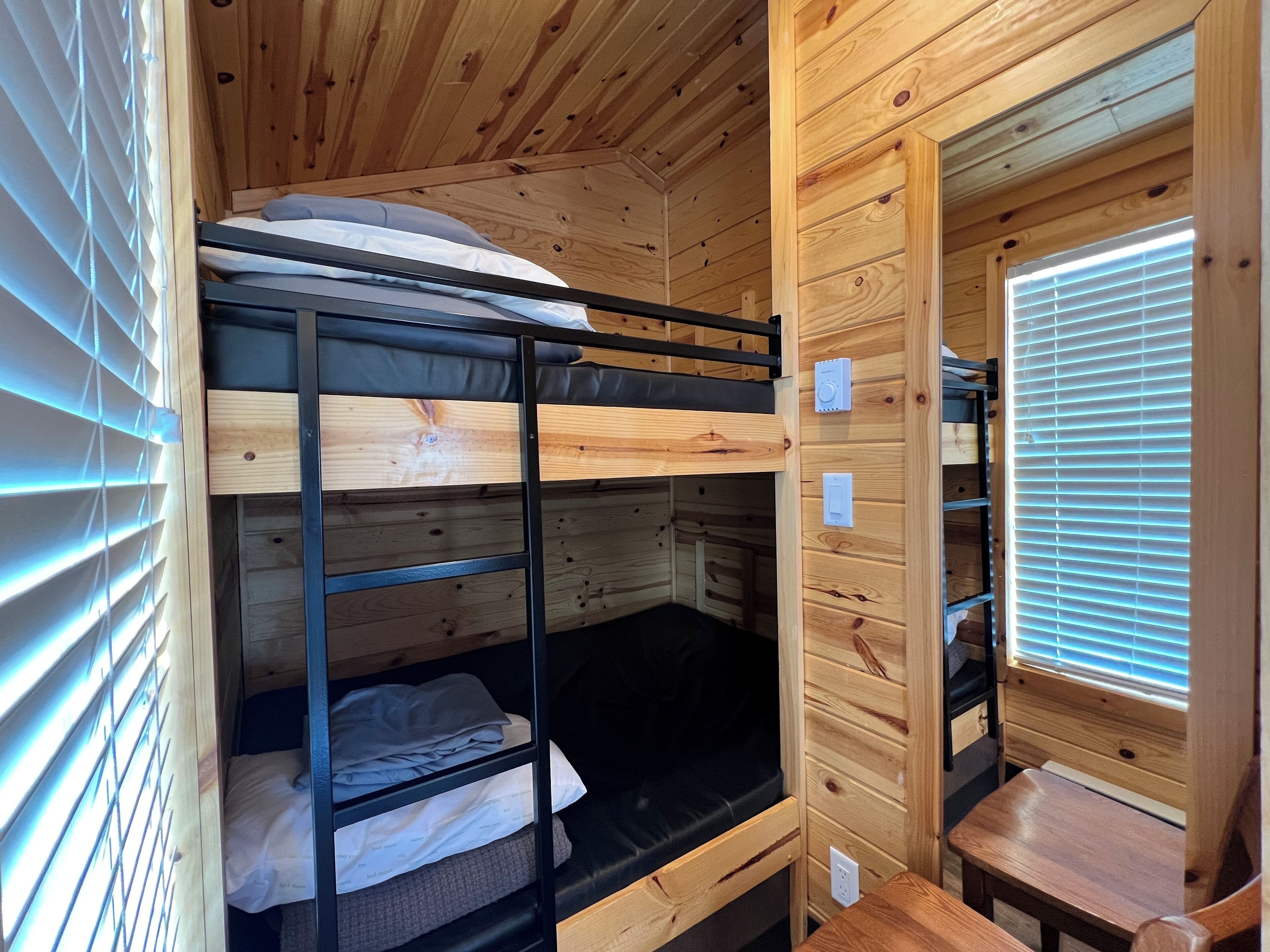 A bunk bed room with wooden walls and a window with blinds.