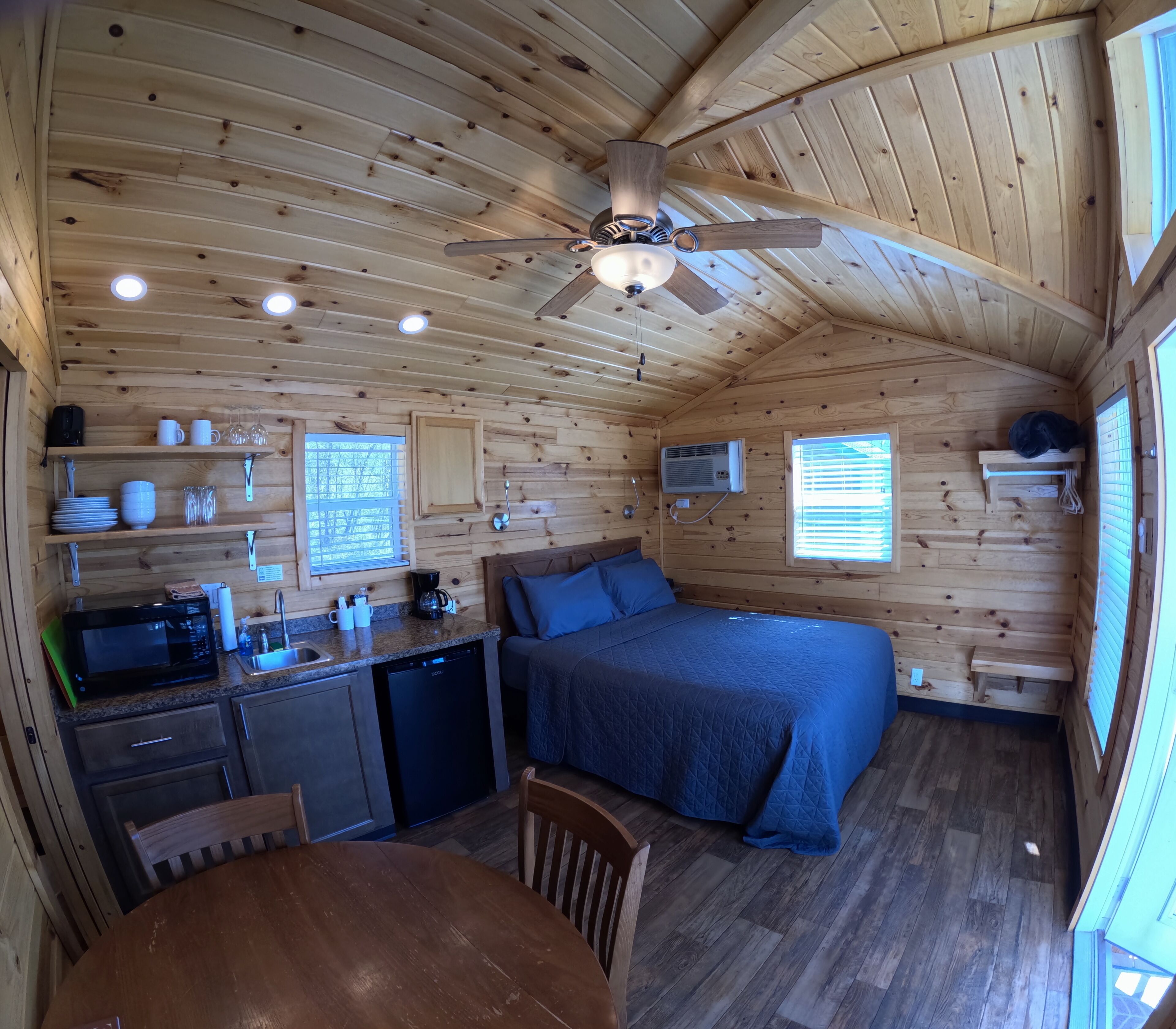 A cozy cabin interior with a bed, kitchenette, and a ceiling fan.
