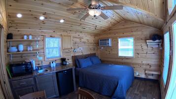 A cozy cabin interior with a bed, kitchenette, and a ceiling fan.