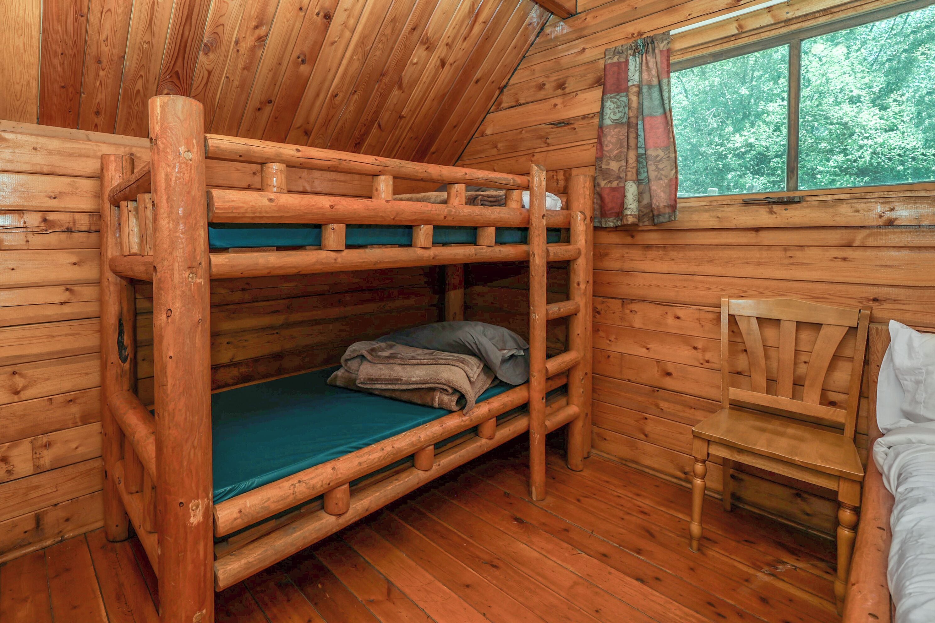 A bunk bed room with wooden walls and a window with curtains.