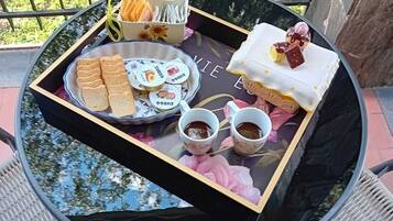 Taula rodona amb safata de petits aperitius, un pastís i dues tasses de te, situada en un balcó amb vista a zones verdes.