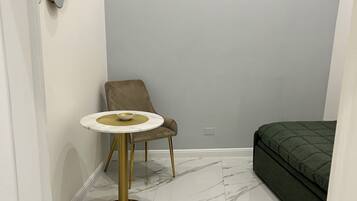 A small, modern room with a round table, a single chair, a bed, and a wall-mounted mirror.