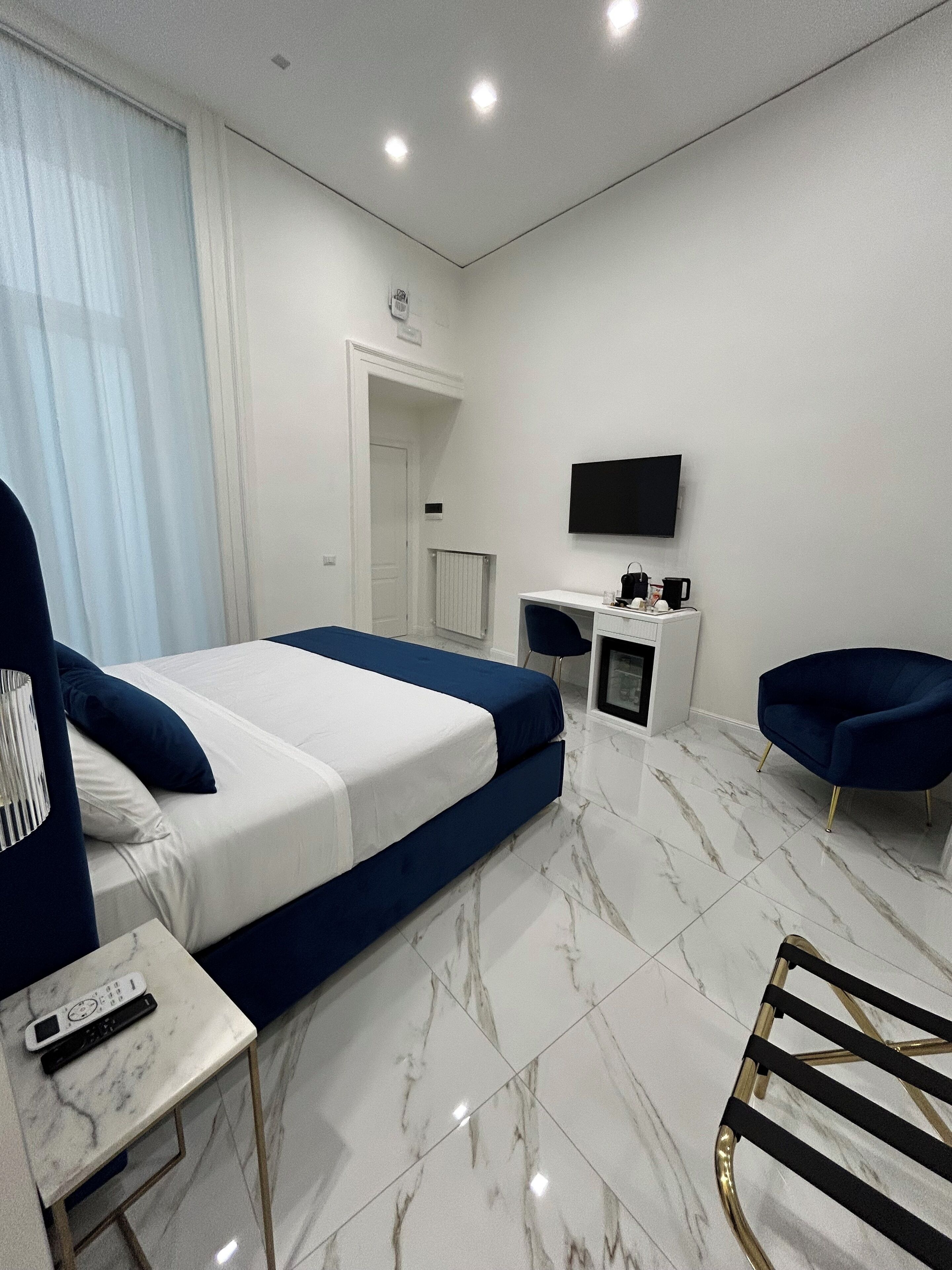 A modern hotel room with a bed, a desk, a chair, a TV, and a small table with a remote control.
