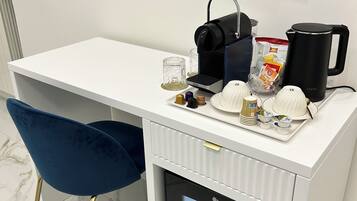 A compact kitchenette with a coffee maker, kettle, and storage for condiments.
