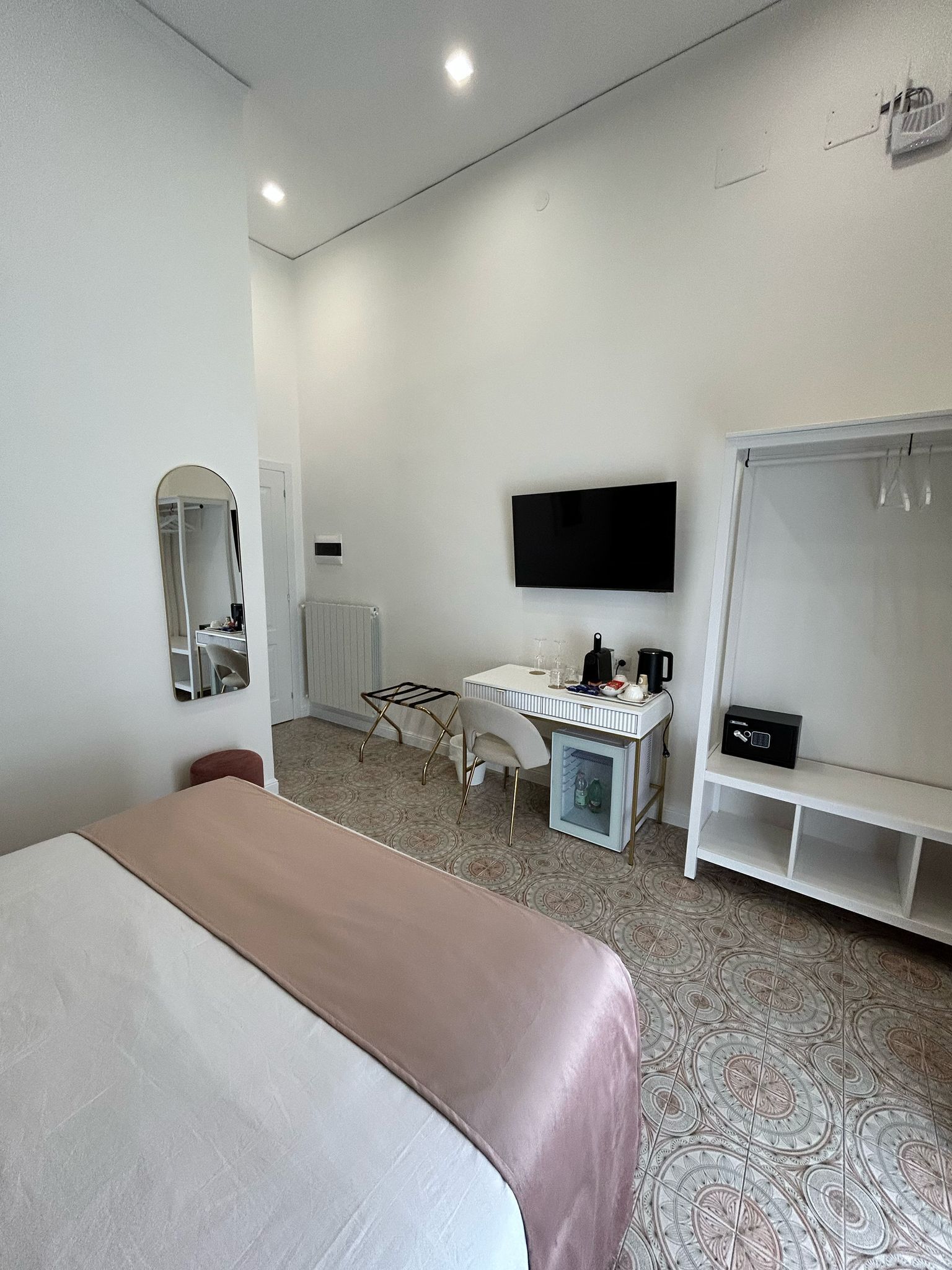 A hotel room with a bed, a desk with a chair, a television mounted on the wall, and a wardrobe.