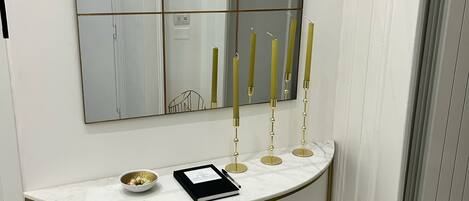 A white console table with a gold frame, a mirror above it, and four candles on the table.