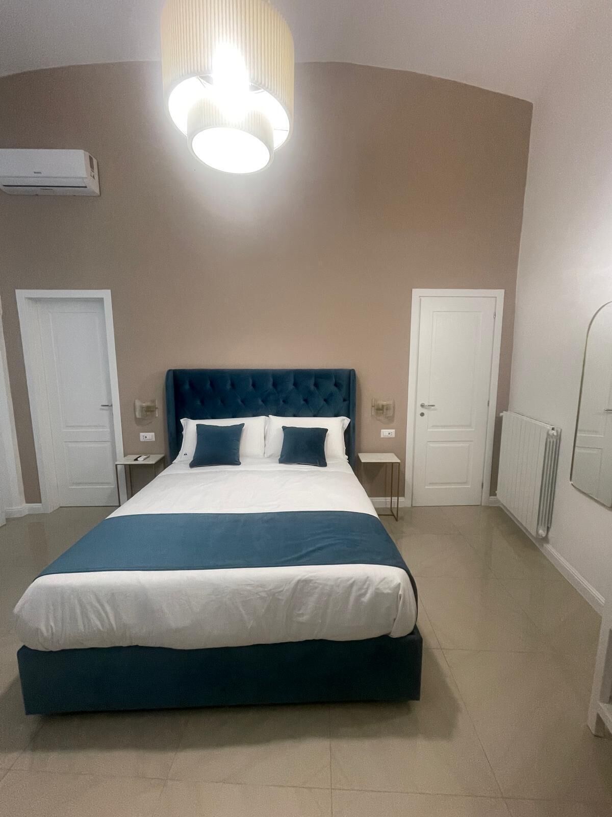Un dormitorio con una cama grande, dos mesitas de noche, un aire acondicionado instalado en la pared y una lámpara en el techo.