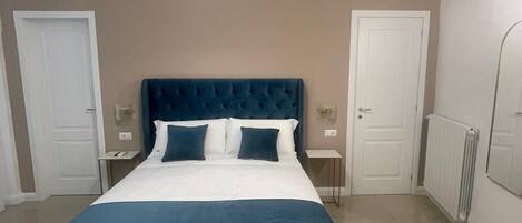 A bedroom with a large bed, two bedside tables, a wall-mounted air conditioner, and a ceiling light fixture.