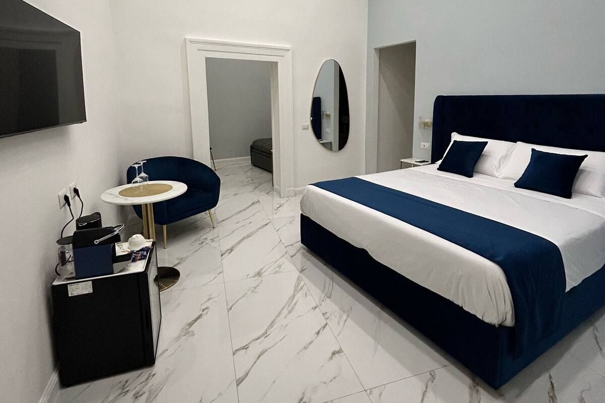 A modern bedroom with a large bed, a small round table, a chair, and a TV mounted on the wall.