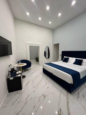 Une chambre moderne avec un grand lit, une petite table ronde, une chaise et un téléviseur fixé au mur.