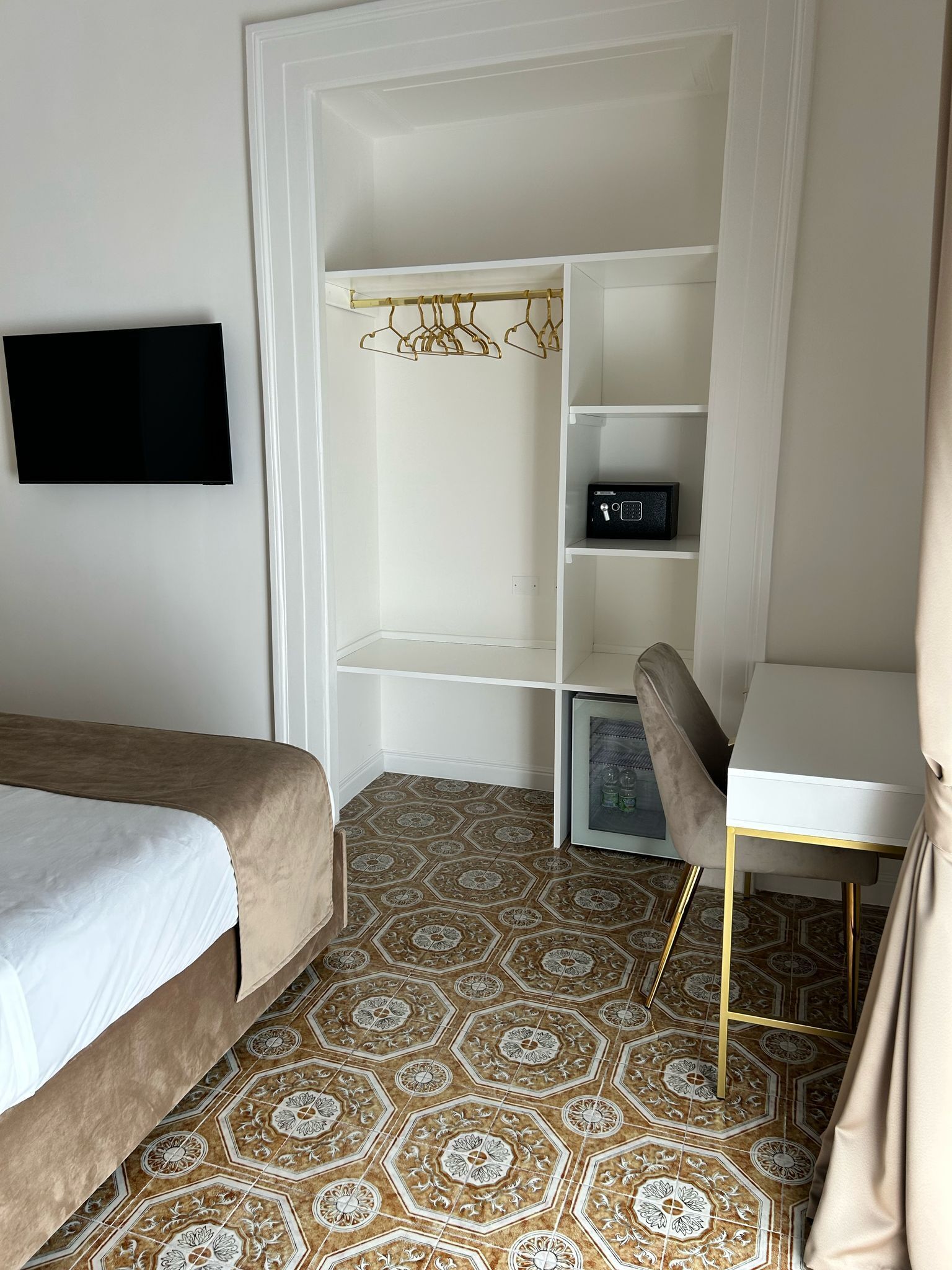 A bedroom with a bed, a desk, a chair, a wardrobe, and a television.