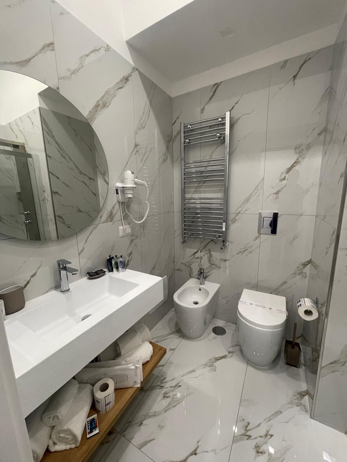 A modern bathroom with a large mirror, a white sink, a bidet, and a toilet.