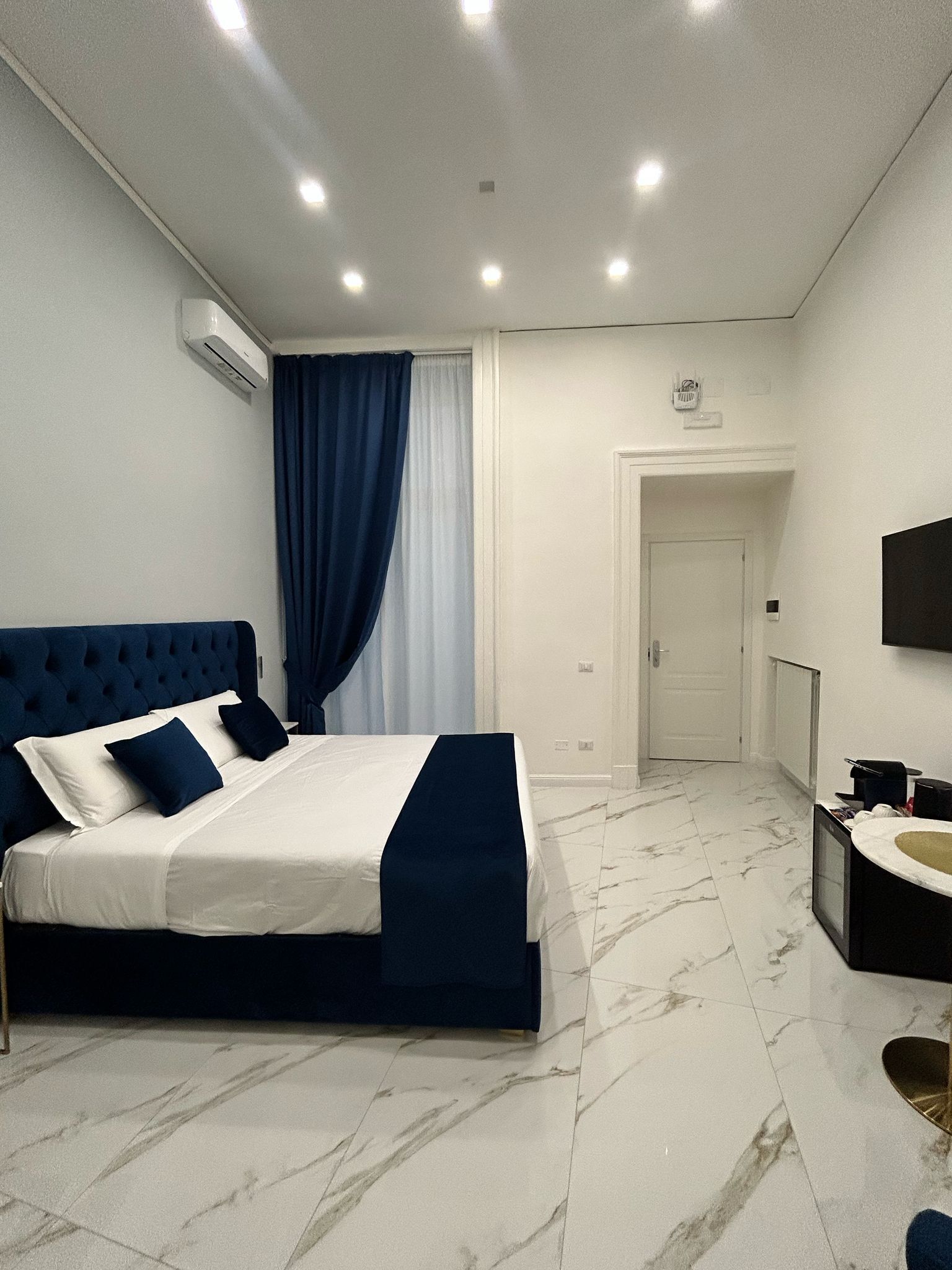 Ein modernes Schlafzimmer mit einem großen Bett, ein Badezimmer mit Waschbecken und Spiegel sowie eine Tür zu einem weiteren Raum.