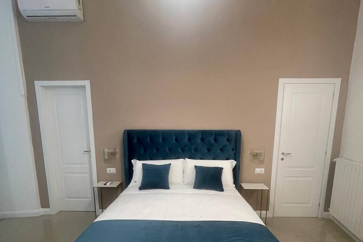 A bedroom with a large bed, two bedside tables, a wall-mounted air conditioner, and a circular light fixture.