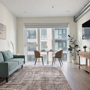 A modern living room with a sofa, two chairs, a small table, and a large window with a view of buildings. - Modern Downtown SLC | King Bed+Pool+Free Parking (Salt Lake City)