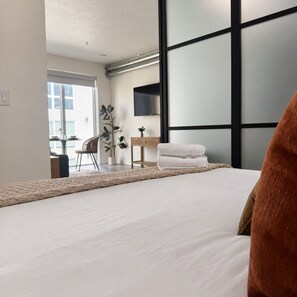 Ein modernes Schlafzimmer mit einem großen Bett, einem Schreibtisch, einem Stuhl und einem Fernseher an der Wand.