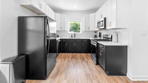 A modern kitchen with white cabinets, a black refrigerator, and a wooden floor. - Cozy & Modern 3BR Houston Townhome - WiFi + AC (Houston)