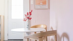 Un comedor con una mesa redonda blanca, una silla de madera y un jarrón con flores rojas.