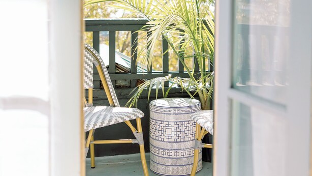 Puerta abierta que da a un patio con una mesa, sillas y una planta en maceta.