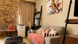 Ein gemütliches Wohnzimmer mit Steinwand, einer Couch, Hocker, einem Sessel und einem Bild an der Wand.