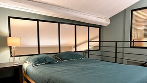 Ein Schlafzimmer mit einem Bett, einem Nachttisch, einer Lampe und einem Fenster mit Jalousien.