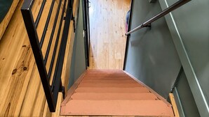 Eine Treppe führt zu einer Ebene darunter, mit Holzboden, Metallgeländer und einem Fenster mit Jalousien.