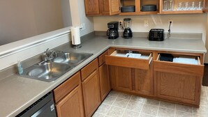 Una cocina con gabinetes de madera, un lavamanos de acero inoxidable, una cafetera, una licuadora y un tostador.