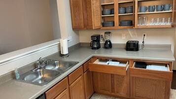 Una cocina con gabinetes de madera, un lavamanos de acero inoxidable, una cafetera, una licuadora y un tostador.
