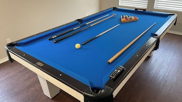 A pool table with a blue felt surface, pool cues, a cue ball, and a set of billiard balls.
