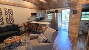 Ein modernes Wohnzimmer mit Sofa, Sessel und Couchtisch, eine Küche mit Kühlschrank und Mikrowelle sowie ein Essbereich mit Barhocker.