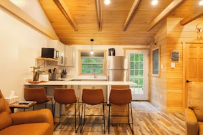 Cocina compacta con refrigerador, microondas y taburetes de bar.