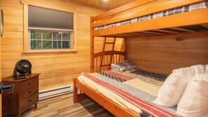 A bunk bed with a wooden headboard, a bedside table with a fan, and a window with blinds.