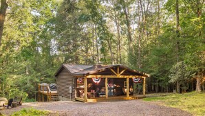 A rustic cabin with a porch, surrounded by a forest.