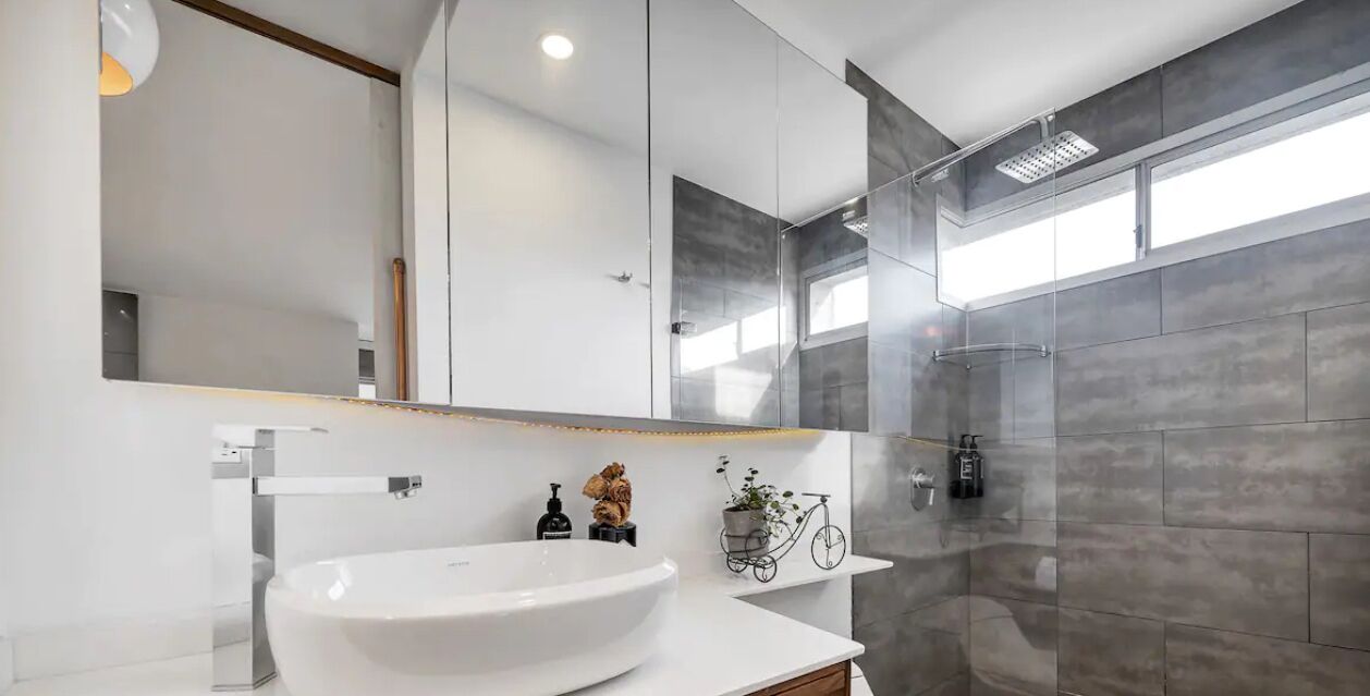 A modern bathroom with a large white sink, a mirror, and a glass shower enclosure.