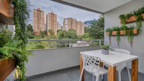 Un balcon avec une table et des chaises blanches, des plantes en pot et une vue sur de hauts immeubles.