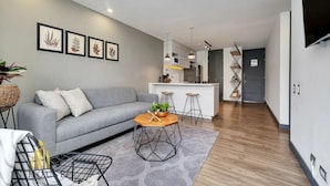 Un salon moderne avec un canapé gris, une table basse et une cuisine en arrière-plan.