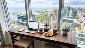 Ett kontor på hög höjd med en bärbar dator, kaffe, bakverk och en krukväxt på ett skrivbord vid ett stort fönster med utsikt över stadsbilden.