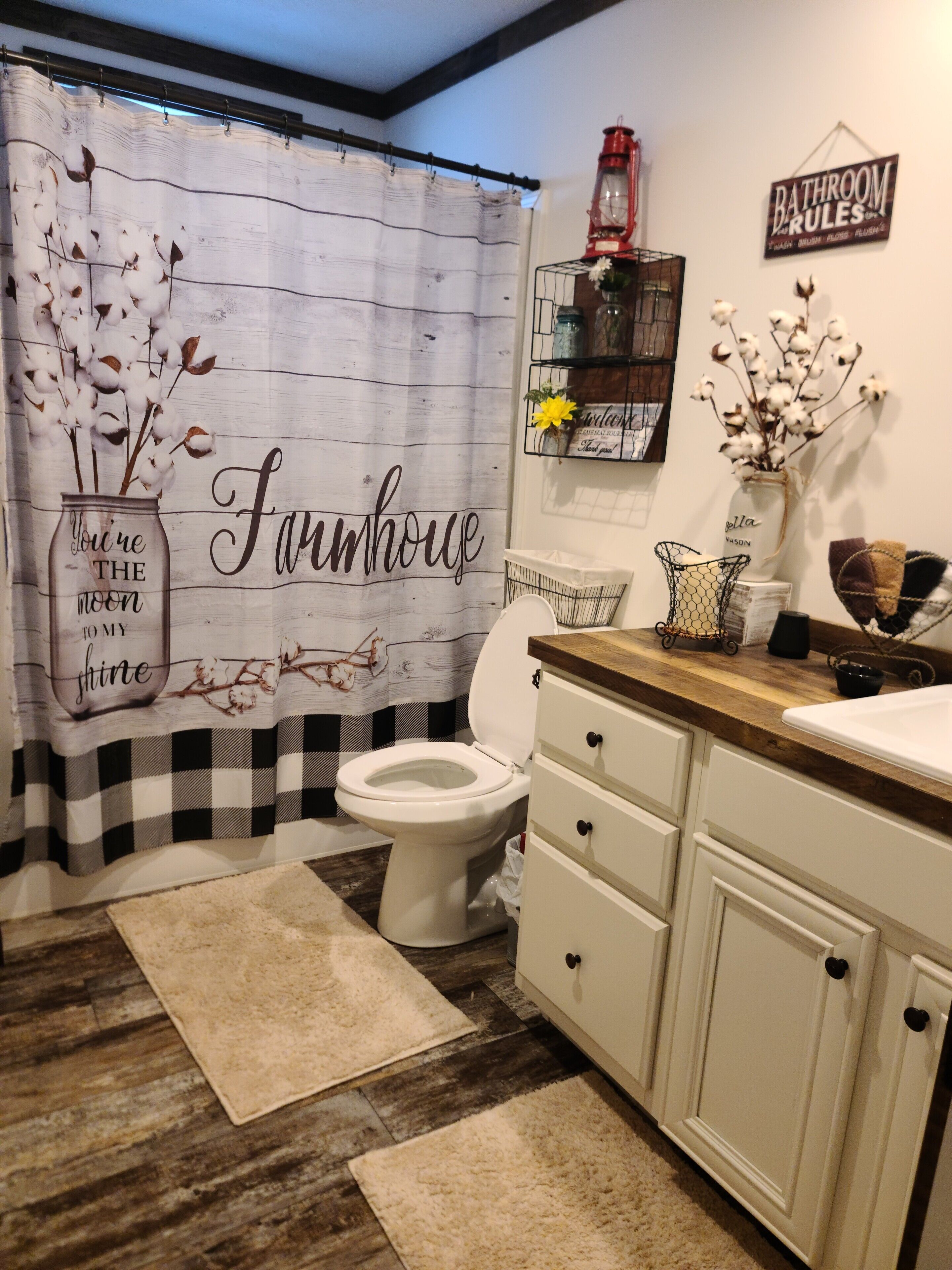 Een badkamer in boerderijstijl, met een zwart-wit geruit douchegordijn, een toilet, een houten wastafelmeubel en een bordje met daarop 'Badkamerregels'.