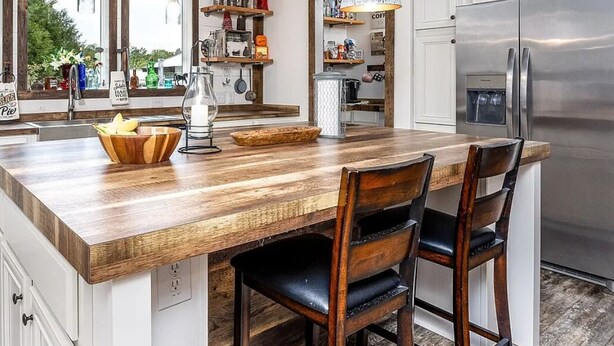 A kitchen with a wooden island, two hanging pendant lights, a stainless steel refrigerator, and wooden cabinets.