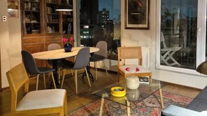 Ein Essbereich mit einem runden Tisch, Stühlen, einer Bücherwand und einem großen Fenster mit Blick auf die Stadt.