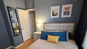 Ein Schlafzimmer mit einem Bett, Nachttischen, einem Spiegel und zwei gerahmten Bildern an der Wand.
