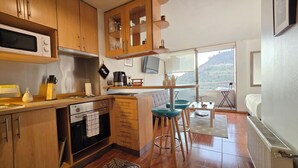 A compact kitchen with wooden cabinets, a built-in microwave, and a stove. There is a dining area with a table and chairs, and a large window offering a view of the outdoors.