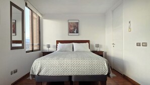 A hotel room with a large bed, two bedside tables with lamps, a framed picture on the wall, and a door with a light switch.
