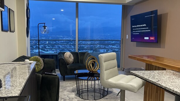 A modern living room with a large window, a TV, and a dining area.