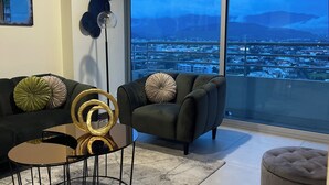 A modern living room with a large window, a black sofa, a round coffee table, and a floor lamp.