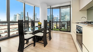 A modern kitchen with large windows, a dining area with chairs, and a view of the cityscape. - Docklands Melbourne CBD Views (Docklands)