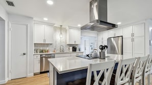 A modern kitchen with white cabinetry, a central island with seating, stainless steel appliances, and a built-in oven. - Stunning 3 BR Oasis with Waterfall Grotto by white sands of Clearwater Beach (Clearwater)
