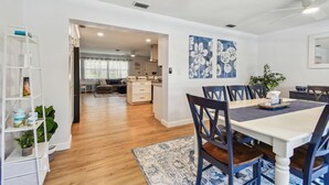 A dining area with a white table and dark chairs, a white shelving unit with decorative items, and a blue floral wall painting. - Stunning 3 BR Oasis with Waterfall Grotto by white sands of Clearwater Beach (Clearwater)