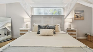 A bedroom with a large bed, bedside lamps, a bedside table, a mirror, and a window with sheer curtains. - Stunning 3 BR Oasis with Waterfall Grotto by white sands of Clearwater Beach (Clearwater)
